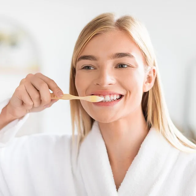 Kvinne med blondt hår og hvit morgenkåpe pusser tenner